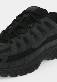 Baskets Nike noires avec un design superposé en mesh et daim, semelle épaisse texturée et lacets noirs.