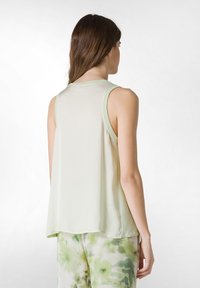 Lys grøn ærmeløs top lavet af blødt stof, med rund halsudskæring og løs pasform for komfort. Kantene er let buede.