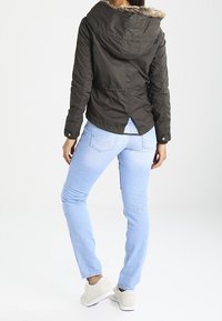 Ciemnozielona kurtka z futrzanym kapturem, dopasowany krój, akcenty z guzikami, połączona z jasnoniebieskimi dżinsami i jasnymi sneakersami.