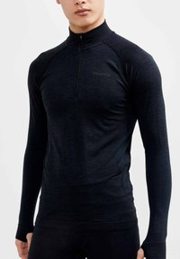 Zwart sportshirt met lange mouwen en een halve rits, gemaakt van rekbare stof, met ribbelaccenten op de mouwen en een logo op de borst.