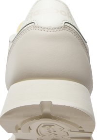 Vue arrière d'une basket blanche Reebok montrant la tige en cuir, les détails de couture et la semelle en caoutchouc texturée avec le logo Reebok.