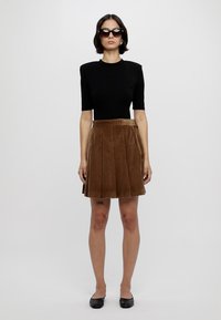 Musthave musta lühikeste varrukatega topp, pruunid korkkangast pliiatsseelikud, mustad ballettpaelad; mudel kannab tumedaid päikeseprille. Sile tekstuur, kohandatud sobivus.