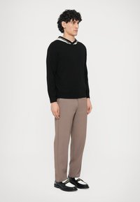 Fekete kötött pulóver csíkos gallérral, bézs szabott nadrág és fekete-fehér mokaszin arany díszítéssel. A modell oldalról áll.