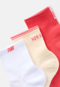 Três pares de meias até ao tornozelo: brancas com o logótipo rosa, creme com "NEW BALANCE" em rosa e vermelhas com uma textura canelada e riscas rosas no topo.