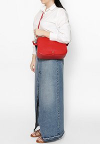 Borsa a spalla in pelle rossa con finitura liscia, dotata di chiusura a pattina e tracolla regolabile. Presentata su uno sfondo neutro.