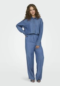 Denimový outfit pozostávajúci z košeľe s gombíkmi a golierom a voľných nohavíc; modrá farba, mäkká textúra a detail elastického pásu.