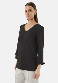 Zwarte V-halsblouse met driekwartmouwen en omslagdetails. Gladde stof met een iets losse pasvorm. Draagt bij lichte gekleurde broeken.