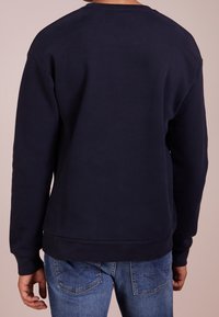 Granatowy sweatshirt z okrągłym dekoltem, długimi rękawami i ściągaczami na mankietach. Gładka tekstura materiału, prosty design, bez widocznych logo i wzorów.