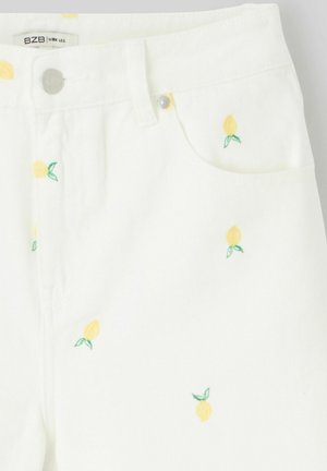 Jean large blanc avec broderie de citron, présentant de petits motifs de citron jaunes avec des feuilles vertes. Fermeture à bouton métallique et zip.