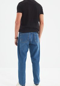 Camiseta oscura de manga corta, combinada con unos vaqueros holgados de color azul claro con un lavado desgastado, bolsillos traseros visibles y costuras mínimas.