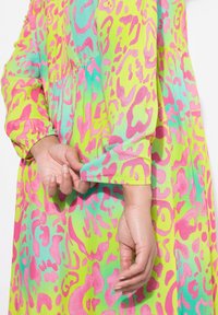 Abito multicolore con sfondo verde brillante, decorato con motivi astratti rosa e blu, maniche lunghe e dettagli arricciati in vita.