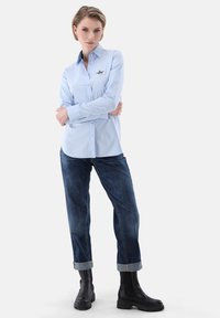 Light blue button-up shirt with a small bird embroidery, paired with dark denim jeans and black ankle boots, featuring cuffed hems.