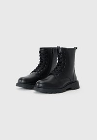 Bottes noires à la cheville avec une finition en cuir lisse, lacées à l'avant et avec une fermeture éclair sur le côté. Elles disposent d'une semelle épaisse et robuste ainsi que d'une languette à l'arrière.
