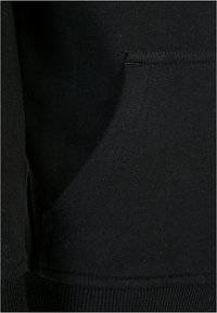 Tejido de sudadera de algodón negro con un bolsillo lateral y dobladillo acanalado. Textura suave con sutiles detalles de costura.