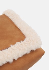 Braune Wildlederhandtasche mit einem flauschigen cremefarbenen Schaffellbesatz, die eine glatte Oberfläche und eine abgerundete Form aufweist. Stichdetails entlang der Kanten.