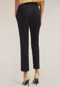 Pantalon noir ajusté avec une coupe slim, doté de deux poches arrière, associé à des chaussures à talons hauts jaunes et un chemisier fleuri.