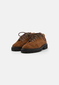Bruine suède wandelschoenen met ronde neus, zwarte rubberen zool en gestructureerde veters. Bevat metalen veterogen en een stevige constructie.