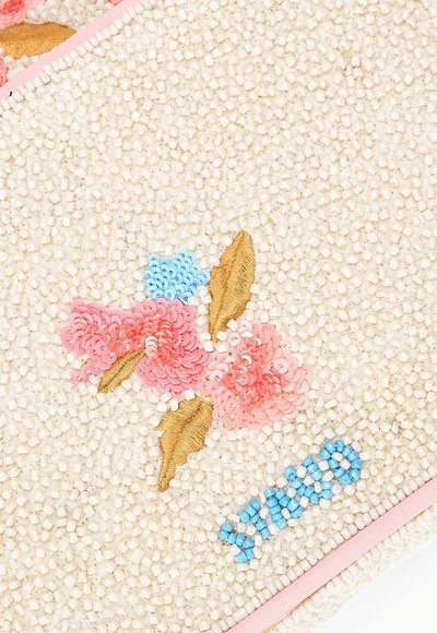 Tissu perlé avec motif floral rose et bleu, feuilles brodées en or et texte perlé bleu "XAVIERI" sur fond crème.