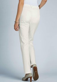 Pantalons blancs à jambe droite avec une texture de tissu lisse, présentant une taille mi-haute et des détails de couture subtils, portés avec des chaussures à talons beiges.