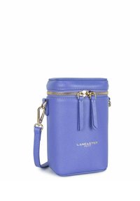 Paarse leren schoudertas met een gestructureerde afwerking, gouden ritssluiting, decoratieve franjes en een merkembleem aan de voorkant. Compact cilindrische vorm.