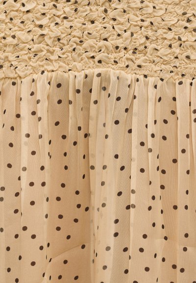 Μπεζ ύφασμα με μαύρες πουά βούλες, που διαθέτει ρυτιδωμένη υφή στο πάνω μέρος και ρέον, πλισέ κάτω τμήμα.