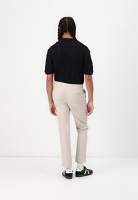 Schwarzes gestricktes Kurzarmoberteil kombiniert mit hellbeigen, schmal geschnittenen Hosen und schwarzen Sneakern, die ein strukturiertes, geschichtetes Design präsentieren.