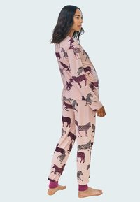 Langärmliges Pyjama-Set aus pinkem Stoff mit einem Zebramuster. Die Hose hat gerippte lila Bündchen. Weiche, glatte Textur.