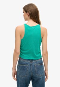 Groene mouwloze crop top van zachte stof, gecombineerd met hoge blauwe denim jeans met achterzakken en een labeldetail.