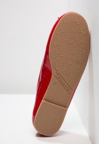 Chaussure plate rouge avec semelle beige texturée affichant le nom de la marque Tamaris et la pointure 37, positionnée à la verticale sur un fond blanc.