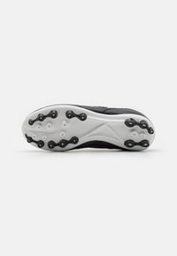 Suela de zapato deportivo negro con clavos de plástico moldeado, entresuela blanca y patrón texturizado para tracción. Superficie plana, diseño minimalista.