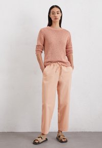 Pull en maille rose clair avec un col rond et des manches longues, associé à un pantalon pêche ample et des sandales marron.