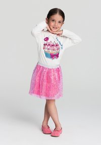 Biała koszula z długim rękawem z grafiką babeczki, zestawiona z różową spódnicą wyszywaną cekinami. Różowe miękkie buty dopełniają strój.