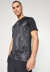 Camiseta deportiva negra con una textura sutil, con patrones verticales del logo de Nike. Mangas cortas y un diseño ajustado.
