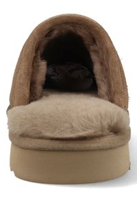 Bruine suede pantoffel met een zachte nep bontvoering en een platte, stevige zool. Het ontwerp is rond met een iets verhoogde achterkant.