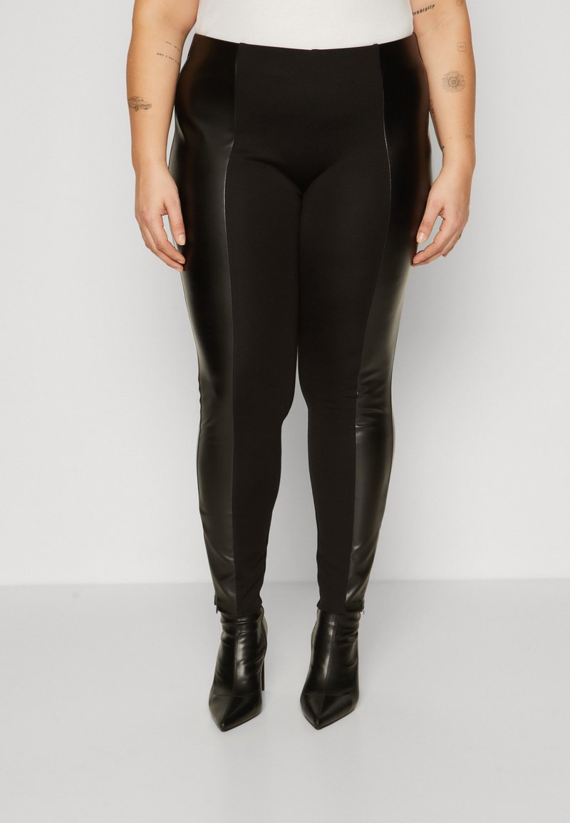 Black leggings featuring faux leather side panels, a stretchy fabric design, high waist, and paired with pointed toe black heels.