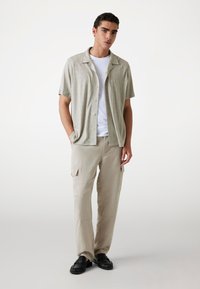 Short-sleeve, light grey button-up shirt with a textured pattern over a white t-shirt. Paired with beige cargo pants and black slip-on shoes.