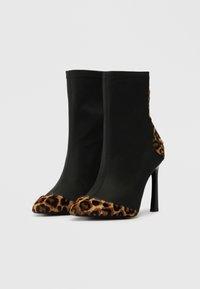 Bottines noires avec un dessus en tissu élégant et un capuchon en fourrure imprimé léopard. Le design présente un talon aiguille et des accents latéraux contrastants.