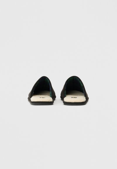 Un par de zapatillas de casa negras sin cordones con forro de felpa blanca y un interior de cuadros verde oscuro, vistas desde el frente.