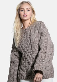 Przesadnie duży sweter z grubym splotem w kolorze taupe, z teksturowanymi wzorami, szerokimi rękawami i ściągaczem u dołu, wykonany z grubej przędzy.