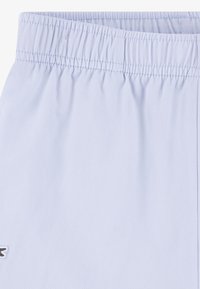 Shorts de sport bleu clair avec une taille élastique, en tissu texturé et un petit logo sur le bas gauche.
