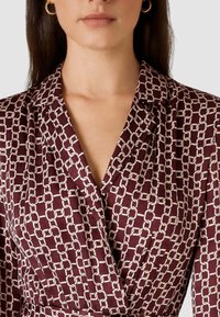 Abito bordeaux con motivo a catena bianca. Presenta un colletto e dettagli plissettati. Realizzato in tessuto liscio e leggero.