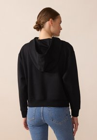 Felpa nera corta con cappuccio regolabile, texture morbida e polsini a coste, abbinata a jeans blu a vita alta. Design semplice e versatile.