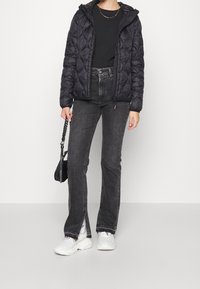 Czarna kurtka puchowa z pikowanym wzorem, zestawiona z ciemnoszarymi jeansami z wysokim stanem i bocznymi rozcięciami oraz białymi trampkami. Dodatkiem jest mała czarna torebka.