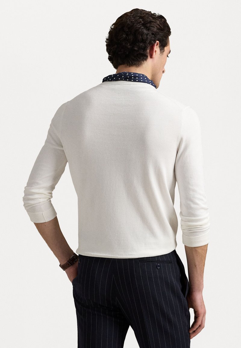 Suéter blanco de manga larga con un cuello de lunares azul marino, cuenta con puños acanalados y un corte relajado. Combinado con pantalones a rayas.