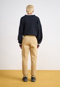 Czarna bluza o luźnym kroju z ściągaczami na rękawach, zestawiona z beżowymi zwężanymi spodniami dresowymi z elastycznym paskiem oraz czarnymi sneakersami.