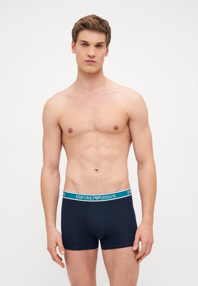 Mornarsko plavi bokserice izrađene od mekog materijala, s tirkiznim pojasom na kojem je logo "Emporio Armani". Pristajanje je usko s dizajnom srednjeg struka.