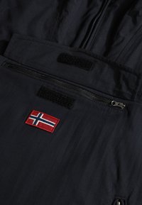 Marinblå vinterjacka med dragkedjefickor, kardborreknäppning och en broderad norsk flagga. Tillverkad av ett slätt och hållbart tyg.