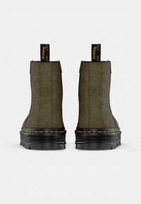 Bottines vertes avec une texture lisse, dotées d'une semelle noire épaisse et de coutures jaunes. Comprend une languette en tissu noir pour un enfilage facile.