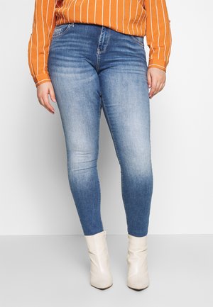 Blauwe denim skinny jeans met een hoge taille en vervagingdetails, gecombineerd met crèmekleurige enkellaarsjes en een oranje gestreept shirt.