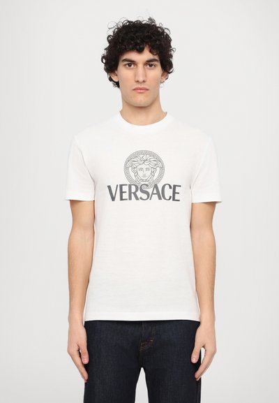 Weißes Baumwoll-T-Shirt mit Rundhalsausschnitt, kurzen Ärmeln und einem zentralen grauen Versace-Logo mit einer Medusa-Grafik in einem gemusterten Kreis.